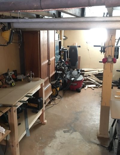 Basement with a tool bench, cabinets, weight set, table saw, and vacuum waiting to be cleaned up for renovations