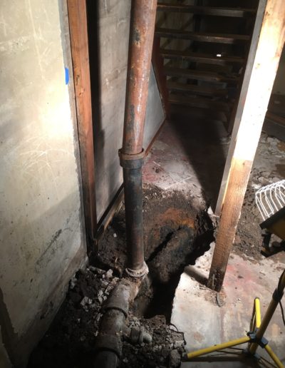A hole in the basement floor dug out around an old cast iron waste stack and additional piping.